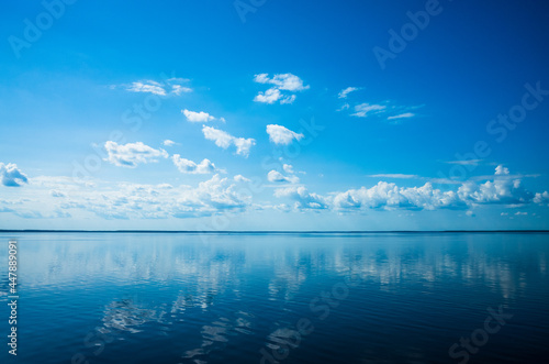 White fluffy clouds blue sky above a surface of the sea. Beautiful sky and ocean using for background. The sky is reflected in the water. Copy space.