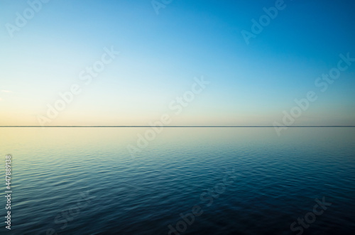 Tranquil minimalist landscape with a smooth blue sea surface with calm waters with a horizon and clear skies. Simple beautiful natural calm background. Copy space.