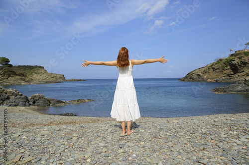 Woman in white dress stretching arms on the beach