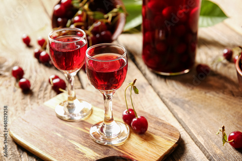 Glasses of sweet cherry wine on wooden background