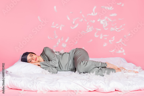 Photo of sweet charming young woman nightwear lying duvet sleeping feather flying isolated pastel pink color background