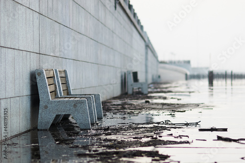 Benches on the granite embankment during the field of flooding with early summer in the morning. Il and branches brought by the river. Selective focus. Blagoveshchensk, Russia.