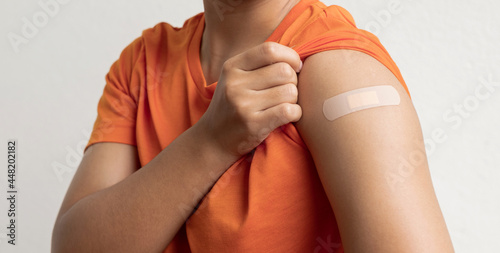 Asian woman shows plaster on her shoulder after being vaccinated against Covid-19. Coronavirus vaccination campaign concept