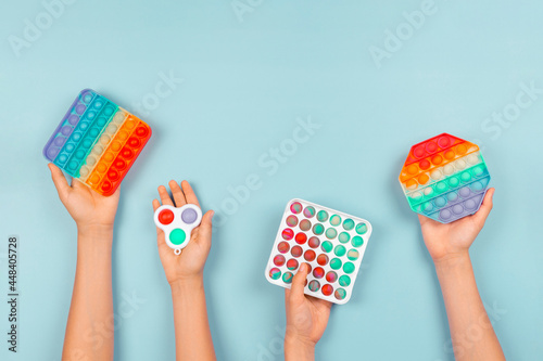 Many hands holding pop it fidget toys on blue background. Push pop-it fidgeting game helps relieve stress, anxiety, autism, provide sensory and tactile experience for children