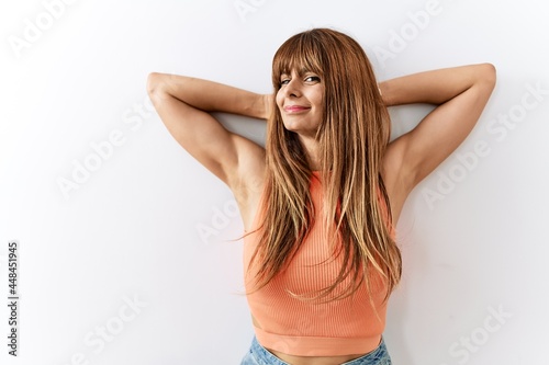 Hispanic woman with bang hairstyle standing over isolated background relaxing and stretching, arms and hands behind head and neck smiling happy
