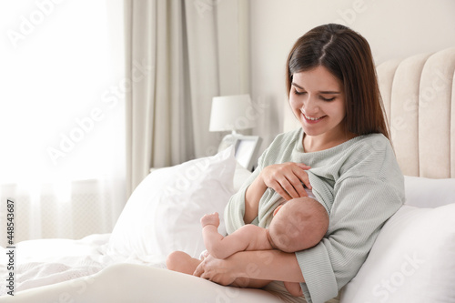 Young woman breastfeeding her little baby on bed at home