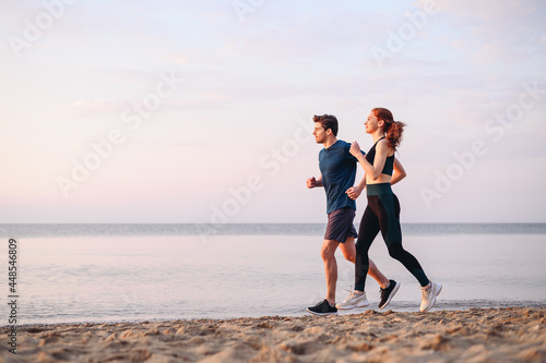 Full body side view couple young two friends strong sporty sportswoman sportsman woman man in sport clothes warm up training run on sand sea ocean beach outdoor jog on seaside in summer day morning.