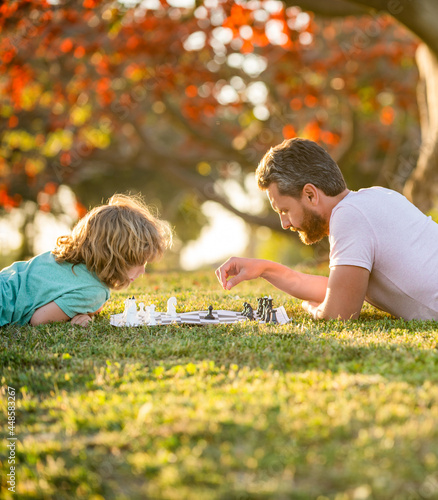 father and son playing chess on green grass. fathers day. happy family. parenthood