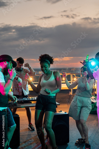 Young dancing friends surrounding African girl during disco at rooftop party