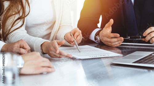 Business people discussing contract while working together in sunny modern office. Unknown businessman and woman with colleagues or lawyers at meeting