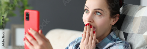 Surprised woman looks at smartphone screen while sitting on couch