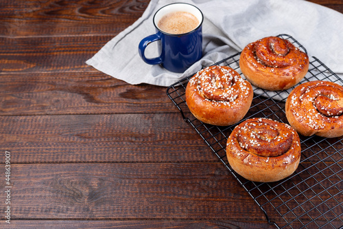 Freshly baked traditional Swedish cinnamon buns Kanelbulle with cup of coffee or cappuccino, on wooden background, horizontal, copy space