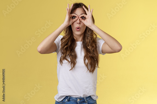 Wow so cool. Girl obersve interesting awesome event show okay perfection gesture look through ring hands folding lips amused wondered glance camera fascinated admiration interested yellow background