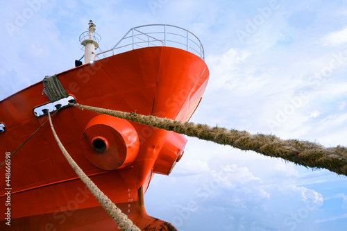 Low angle view of cargo ship docked at port with mooring rope against white clouds on blue sky background