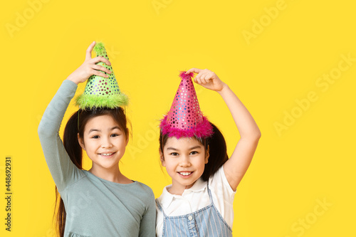 Cute Asian sisters in party hats on color background