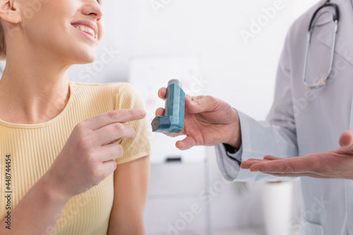 cropped view of asthmatic woman smiling near doctor pointing at inhaler