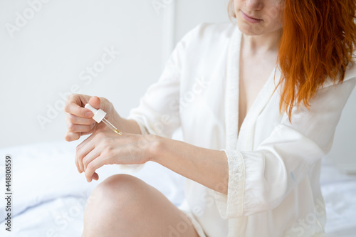 ginger smiling woman middle age in silk robe with cosmetic oil for hands and body in bright room