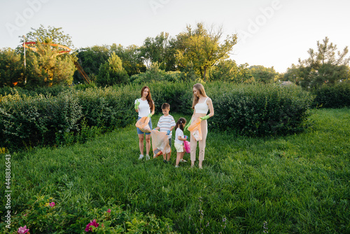 A group of girls with children at sunset are engaged in garbage collection in the park. Environmental care, recycling.