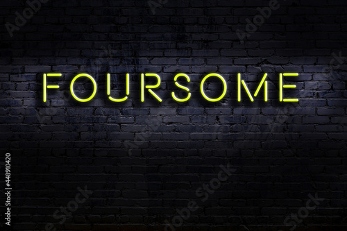Neon sign. Word foursome against brick wall. Night view