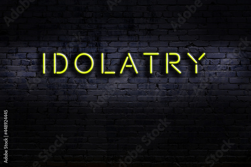 Night view of neon sign on brick wall with inscription idolatry