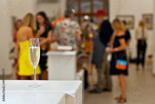 Glasses with wine on the background of the exhibition of paintings. People blurred in the background. Art salon with white walls.