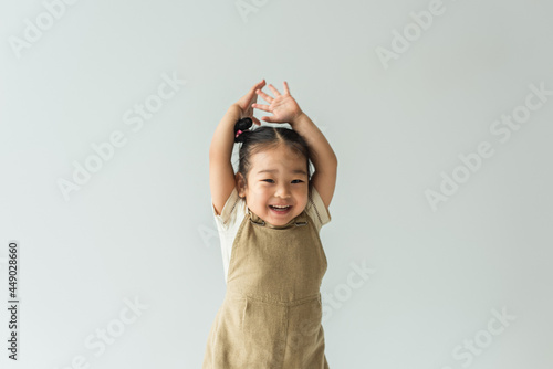 happy asian toddler girl with raised hands isolated on grey