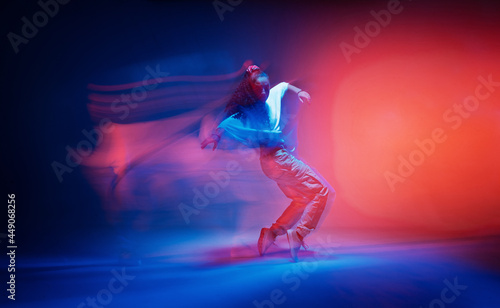 Dancing female standing on tiptoe in colourful neon studio light. Long exposure. Contemporary hip hop dance