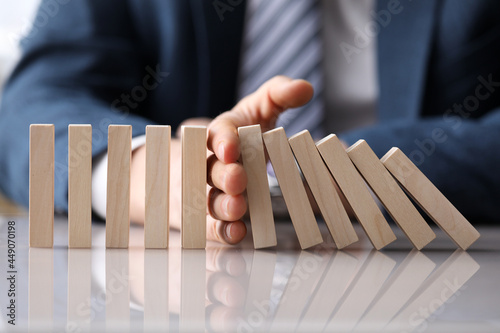 Business man in suit holding with hand falling sequence of wooden blocks