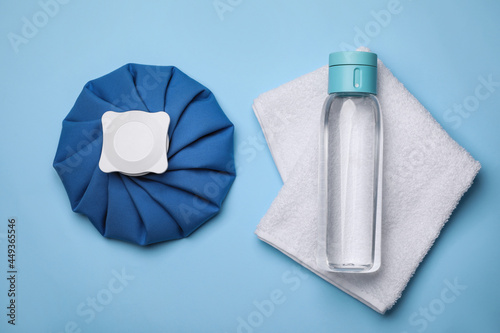 Bottle of water, cold compress and towel on light blue background, flat lay. Heat stroke treatment