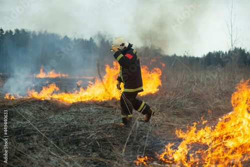 A firefighter extinguishes dry grass. A firefighter is fighting a fire in an open area.