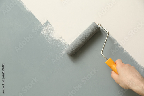 Man applying grey paint with roller brush on white wall, closeup