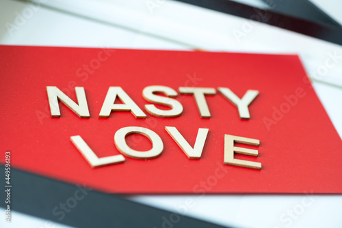 the expression "nasty love" in san serif capital letters on a red background - close up using a macro lens - shallow depth of field (subjective focusing)