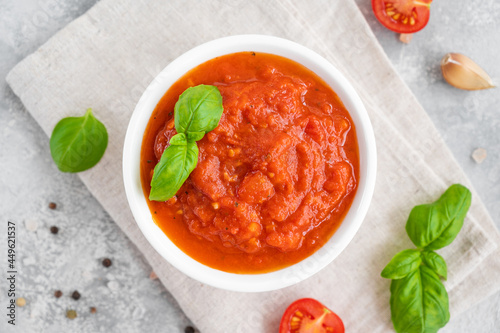 Traditional Italian marinara sauce in a bowl on a concrete background with spices and ingredients. Top view. Copy space.