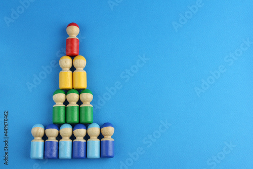pyramid of multicolored wooden toy people on blue background with copy space, concept of social rating