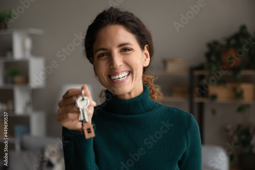 Head shot portrait smiling woman showing keys at camera, purchasing new house, moving into first new apartment, happy young female tenant renter rejoicing relocation, mortgage or rent concept