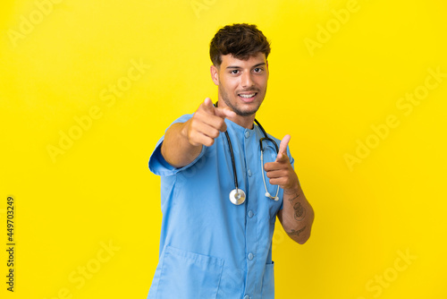 Young surgeon doctor man isolated on yellow background pointing to the front and smiling