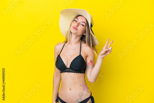 Young Romanian woman isolated on yellow background in swimsuit in summer holidays and doing victory gesture