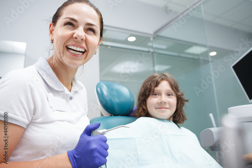 Happy beautiful female dentist laughing while working with child patient at her clinic