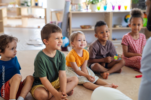 Group of small nursery school children sitting on floor indoors in classroom.