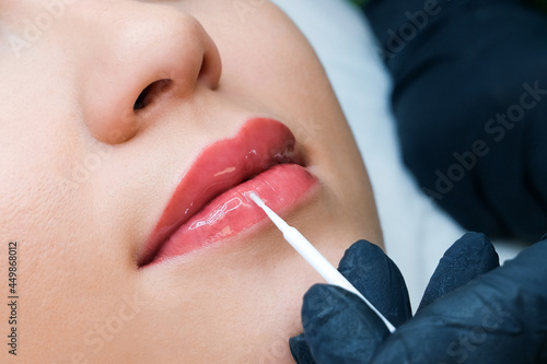 permanent makeup on her lips at the beautician salon. Applying liquid glass to lips