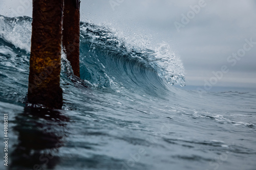 Crashing glassy wave on the beach. Breaking ocean wave and pier