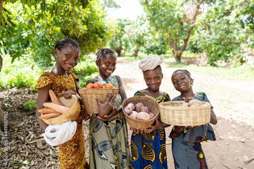 Group of pretty smiling African girls carrying baskets full of vegetables, on their way to the lokal market