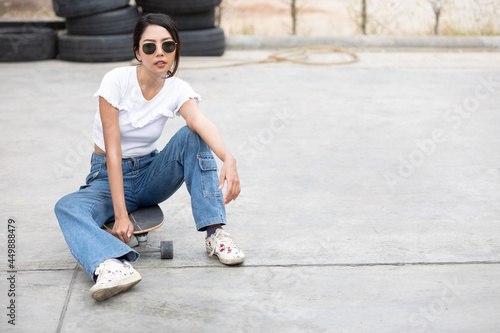 portrait young female skateboarder with sunglasses sitting on skateboard