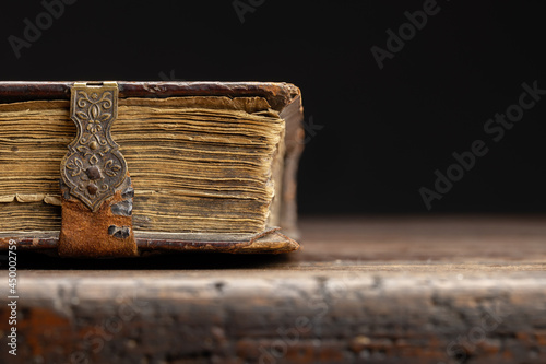 Part of an antique book on a clasp is visible on an old wooden table, close-up.