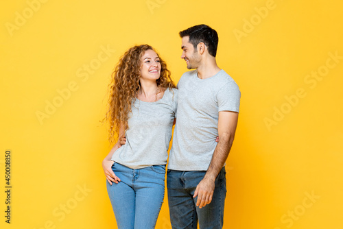 Young happy interracial millennial couple holding and looking each other in the eyes in isolated yellow studio background