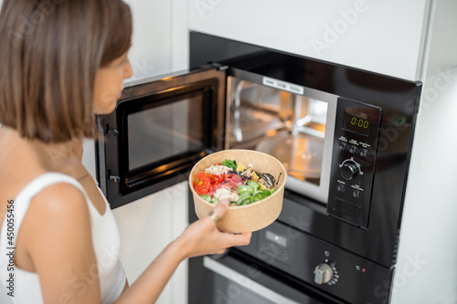 Woman heating food with microwave machine at home, female using modern kitchen appliances