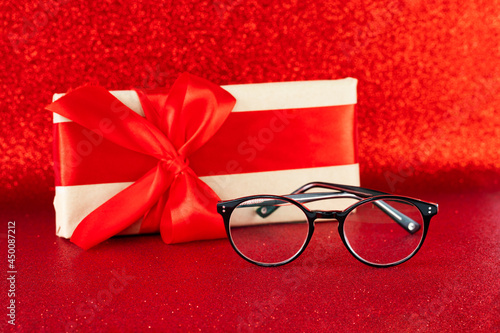 Black eyeglasses on festive red glitter background with a present box