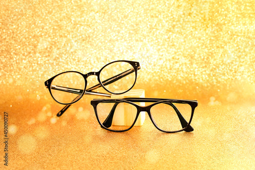 A pair of black eyeglasses on golden glitter background