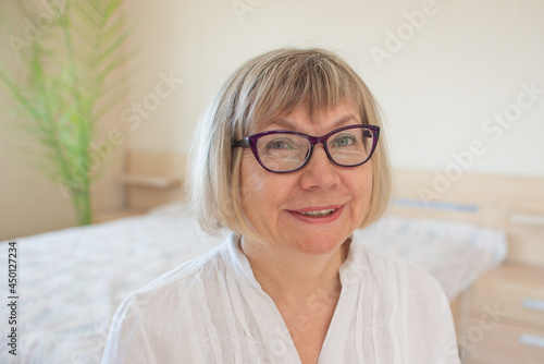 Happy senior woman with gray hair relaxing smiling is looking at the camera in her home in the bedroom