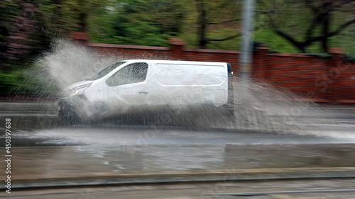 Samochód w czasie ulewy wpada w kałużę wody na jezdni powodując rozbryzg.